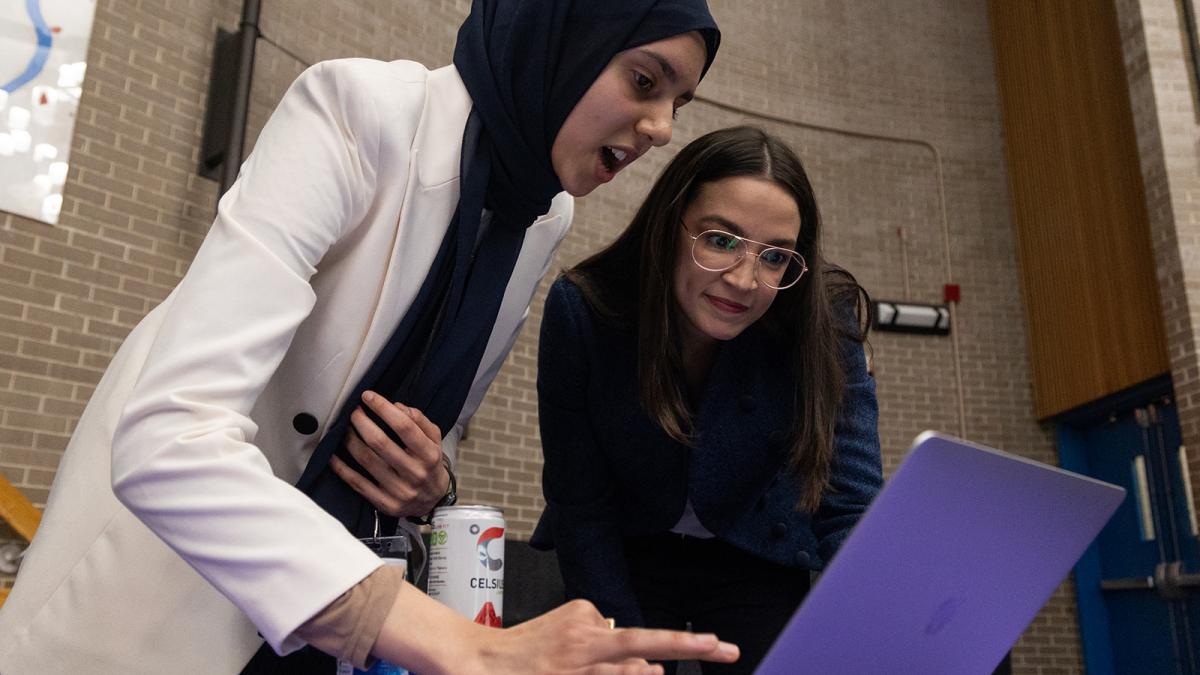 Rep. AOC looks at a computer with a young woman